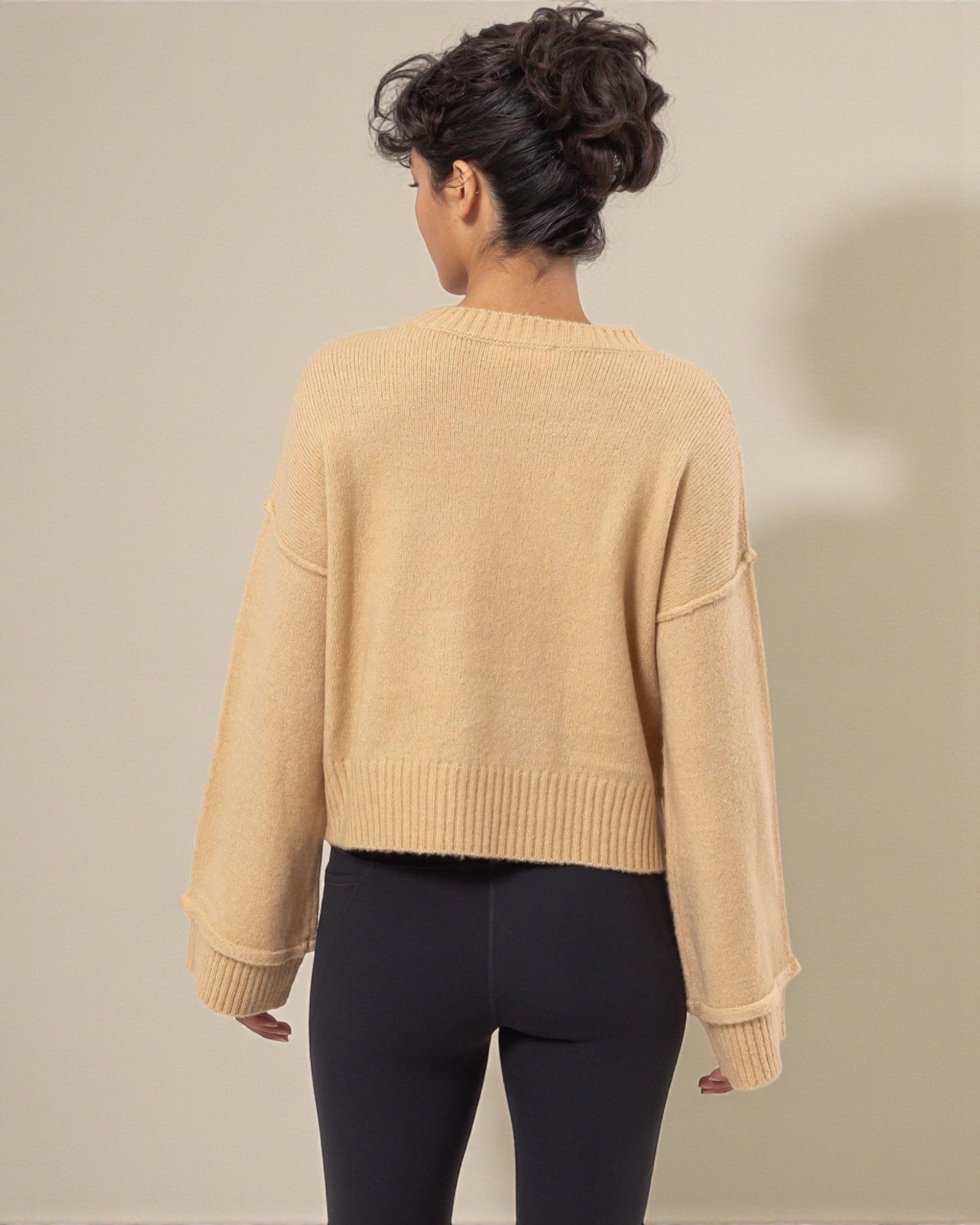 Person wearing a beige sweater and black leggings against a neutral background