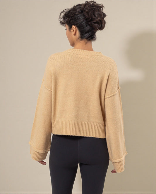 Person wearing a beige sweater and black leggings against a neutral background