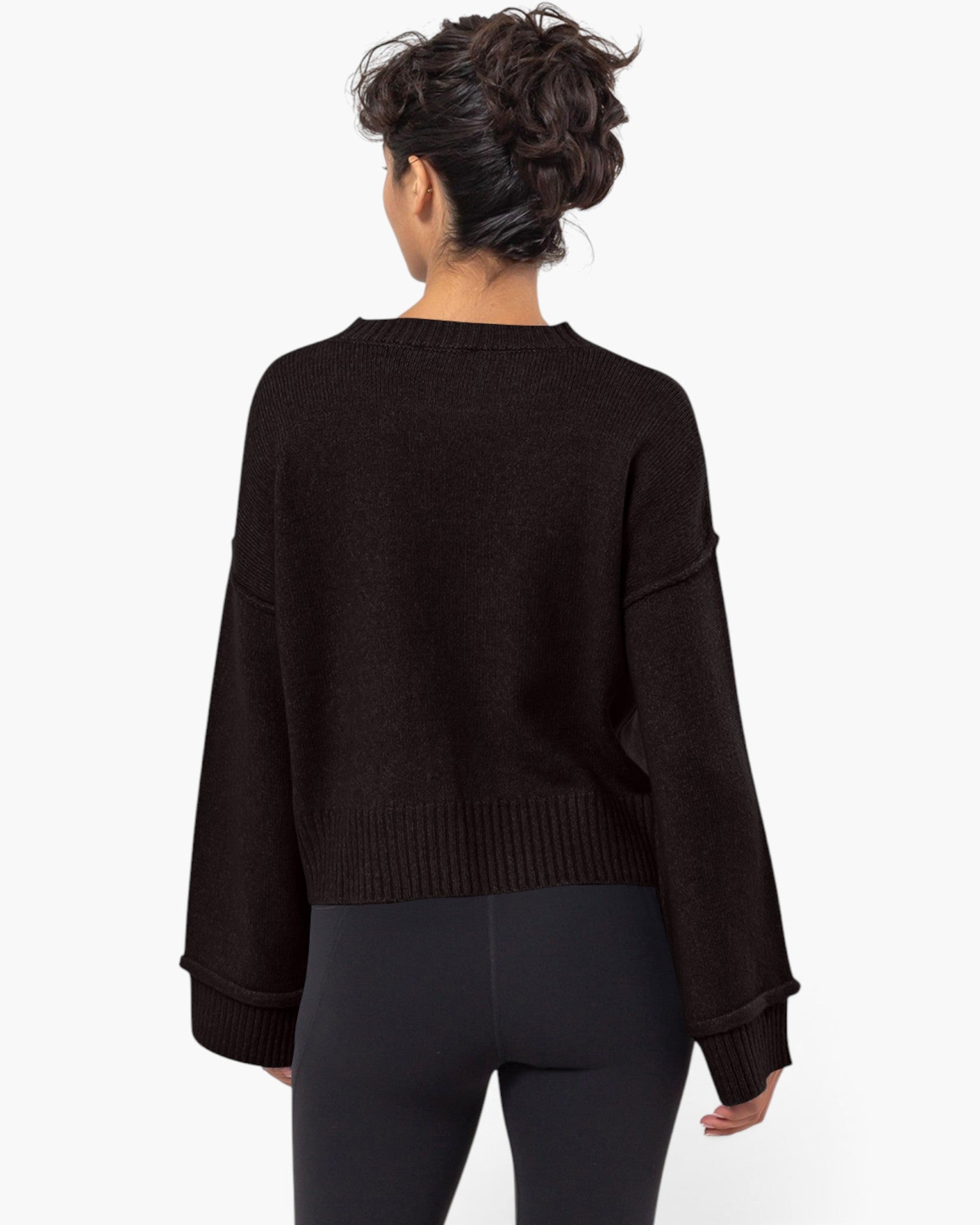 A woman viewed from the back wearing a dark brown long-sleeve knit sweater and black leggings against a plain white studio background.
