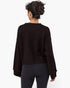 A woman viewed from the back wearing a dark brown long-sleeve knit sweater and black leggings against a plain white studio background.