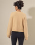 Person wearing a beige sweater and black leggings against a neutral background