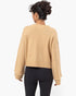 A woman shown from the back wearing a cropped, long-sleeve knit sweater in a warm camel beige color, paired with black leggings, against a plain white background.