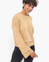 A woman wearing a cropped, long-sleeve knit sweater in a warm camel beige color, paired with black leggings, photographed against a clean white studio background.