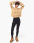 A model wearing a beige cropped knit sweater, black leggings, and tan suede boots, standing against a plain white studio background.