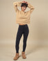 Person wearing a beige sweater, black leggings, and brown boots on a beige background