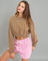 Woman wearing a brown cropped sweatshirt and pink shorts on a gray background