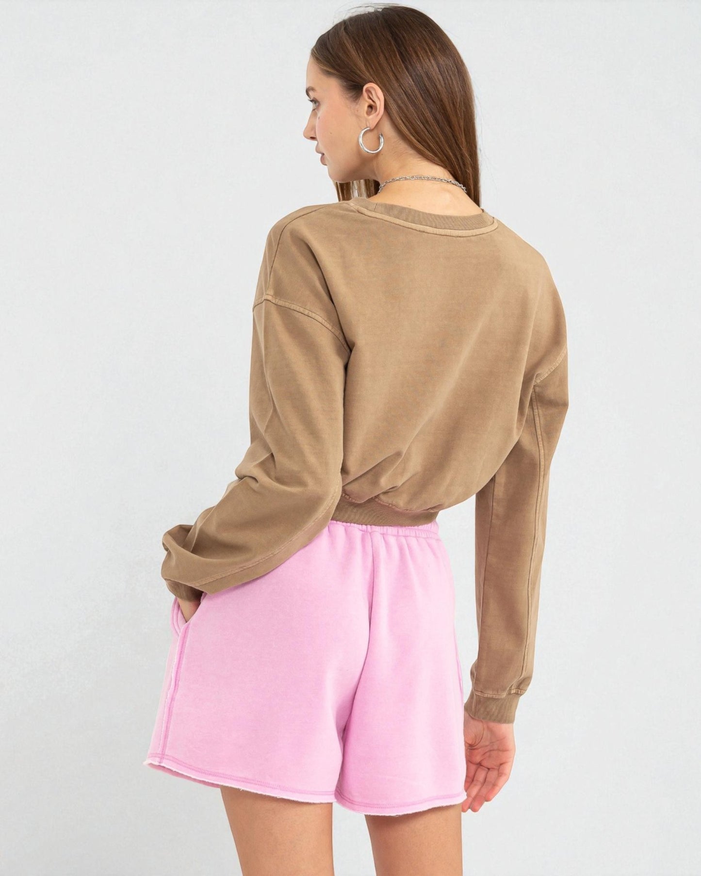 Person wearing a brown long-sleeve top and pink shorts on a white background