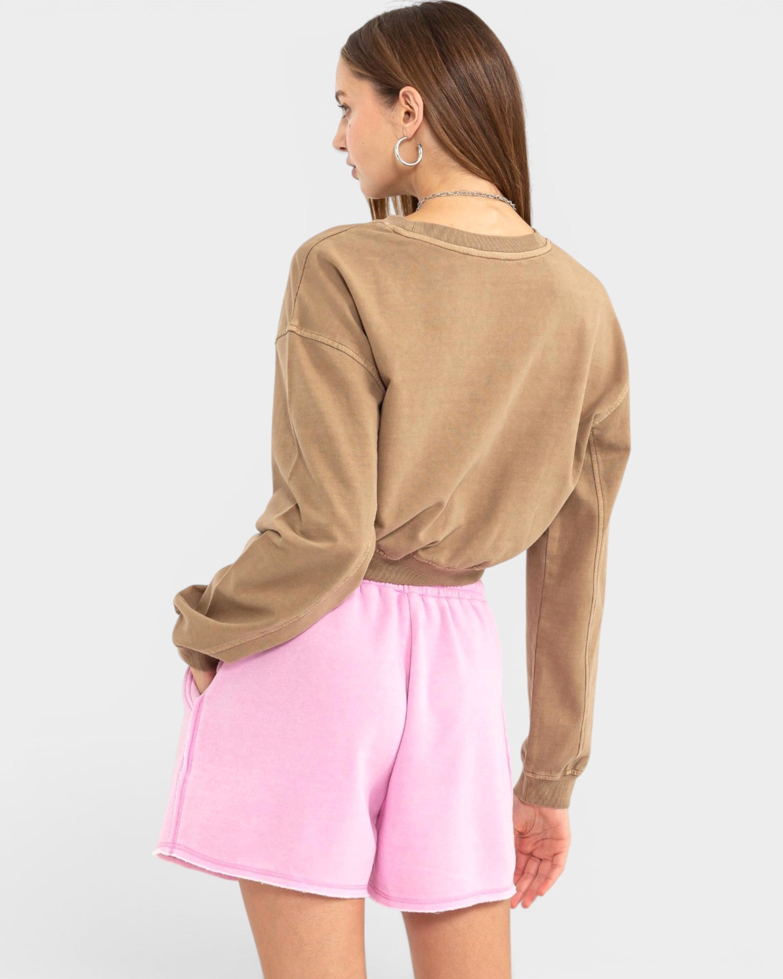 Person wearing a brown sweatshirt and pink shorts on a white background