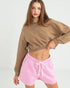 Woman wearing a brown cropped sweatshirt and pink shorts on a white background