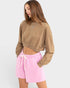 Woman wearing a brown cropped sweatshirt and pink shorts on a white background