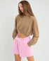 Woman wearing a brown cropped sweatshirt and pink shorts on a white background