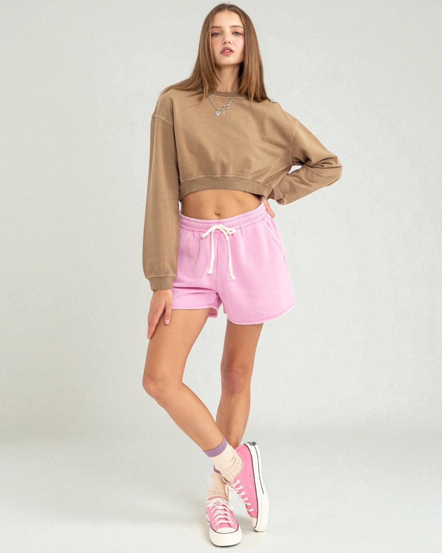 Woman wearing a brown sweatshirt and pink shorts on a white background
