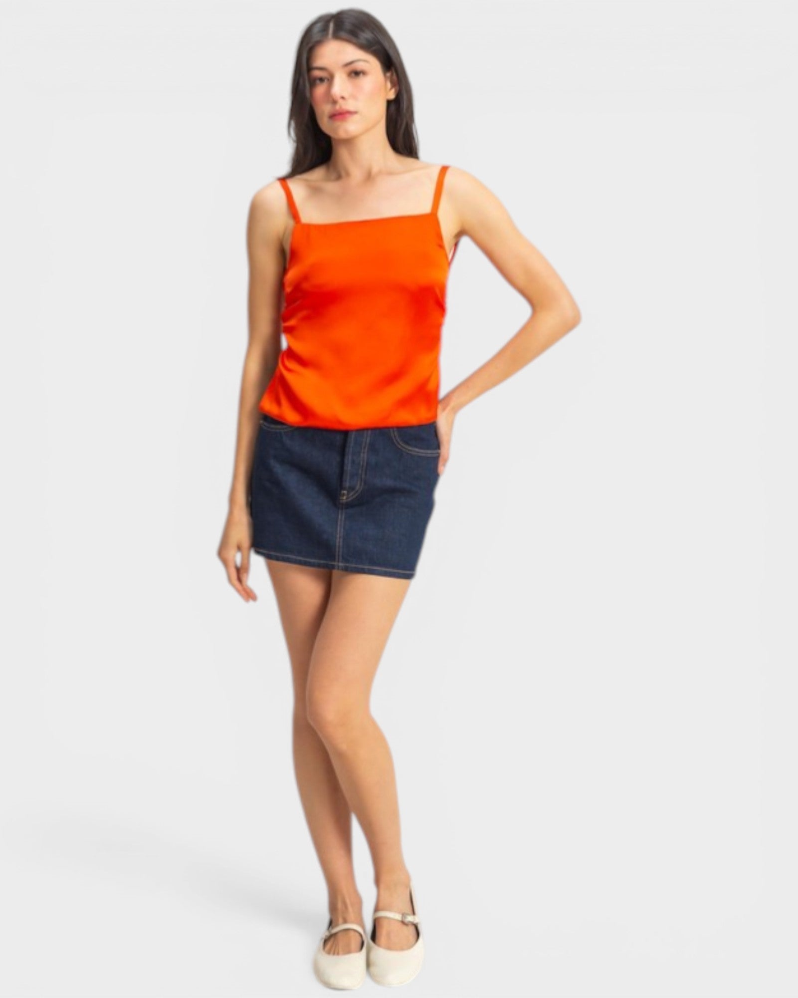 Woman wearing an orange tank top and denim skirt on a white background