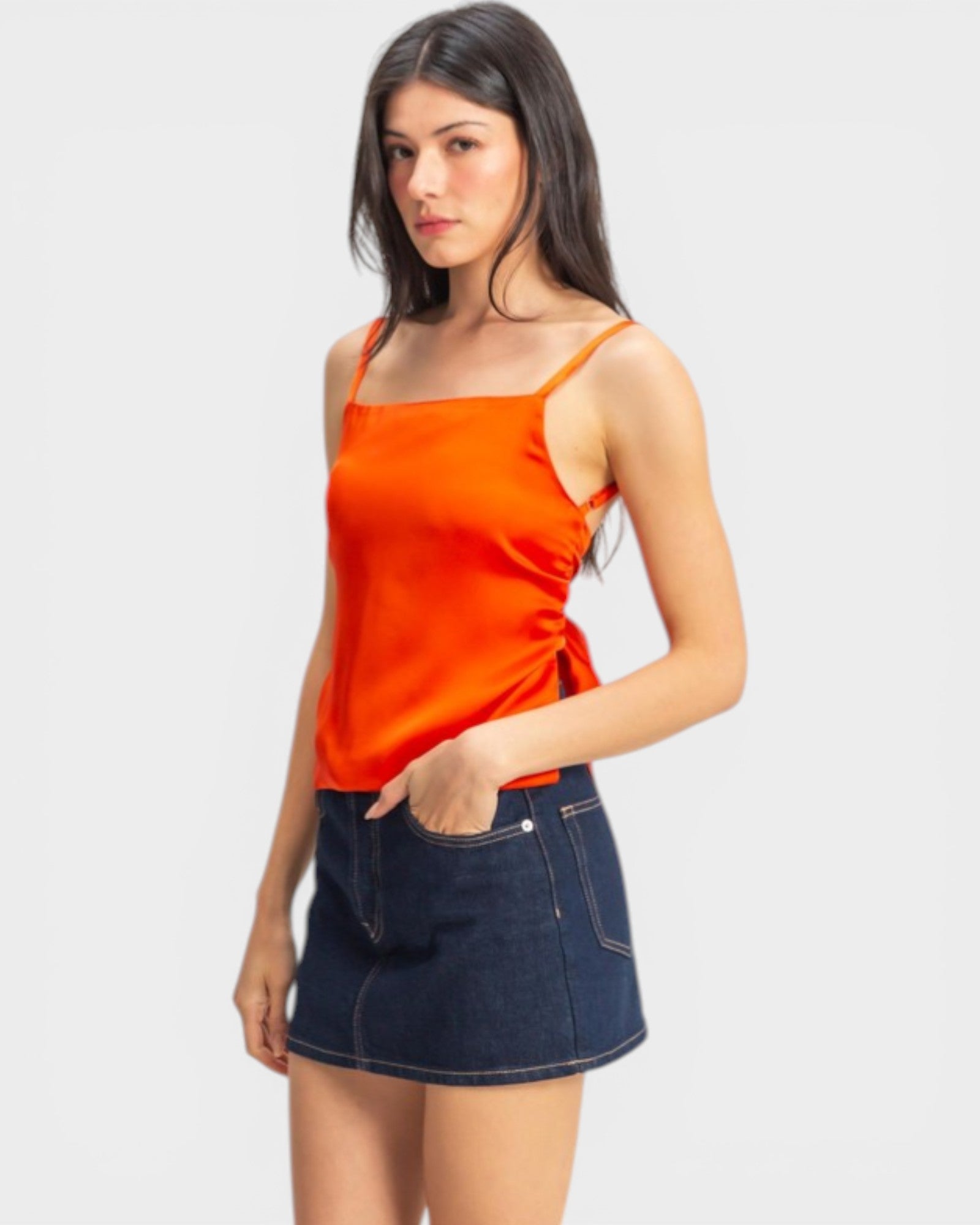 Woman wearing an orange top and denim skirt on a white background