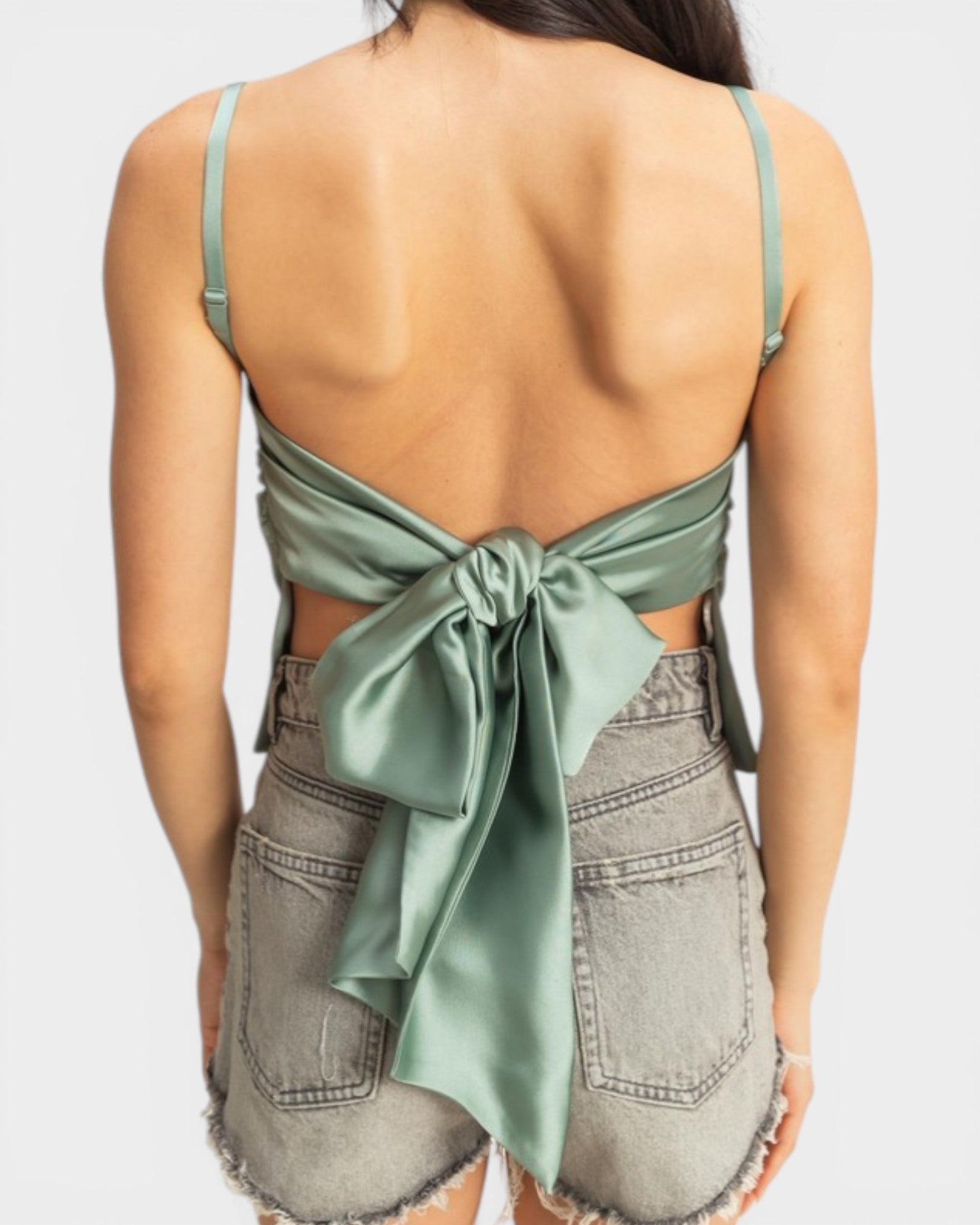 Woman wearing a green open-back top and denim shorts on a white background