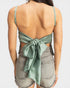 Woman wearing a green open-back top and denim shorts on a white background