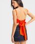 Woman wearing an orange top with a bow detail and denim skirt on a white background