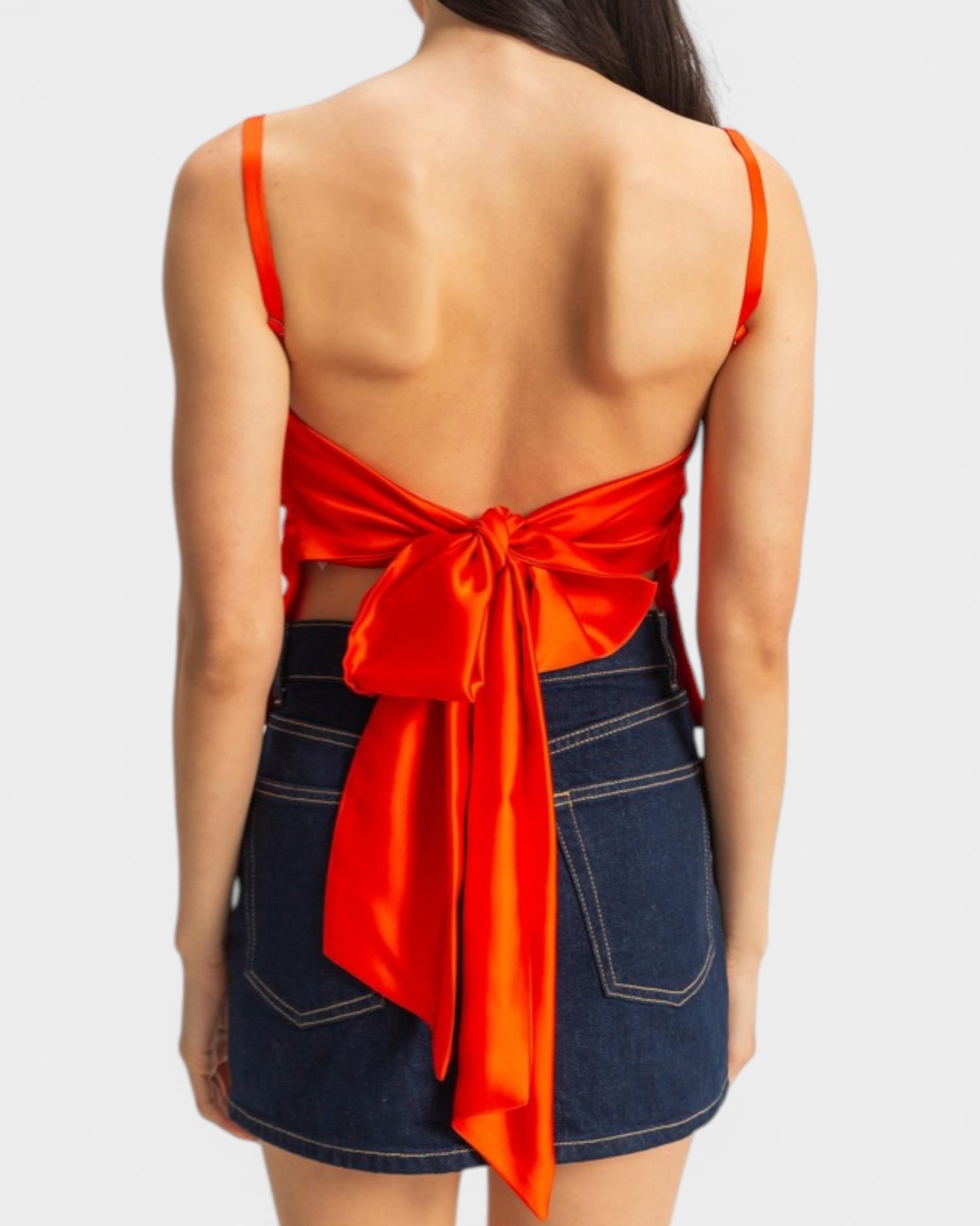 Woman wearing an orange top with a bow and denim skirt on a white background