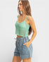 Woman wearing a green crochet top and denim shorts on a white background