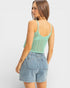 Woman wearing a green crochet tank top and denim shorts on a white background