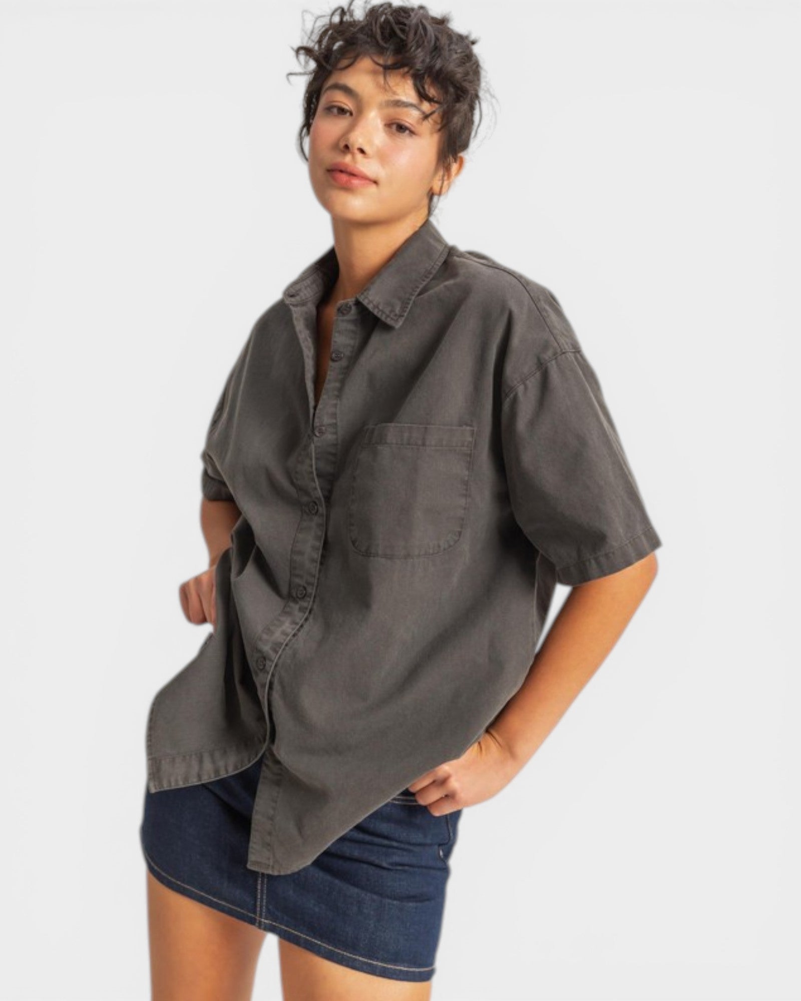 Woman wearing a dark gray oversized shirt over a denim skirt on a white background