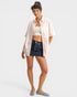 Woman wearing a light pink shirt over a white crop top and dark denim shorts on a white background