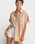 Woman wearing a beige button-up shirt and white shorts on a plain background