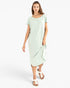 A woman modeling a light mint green short-sleeve midi dress with a draped hem, paired with white flat sandals, against a plain white studio background.