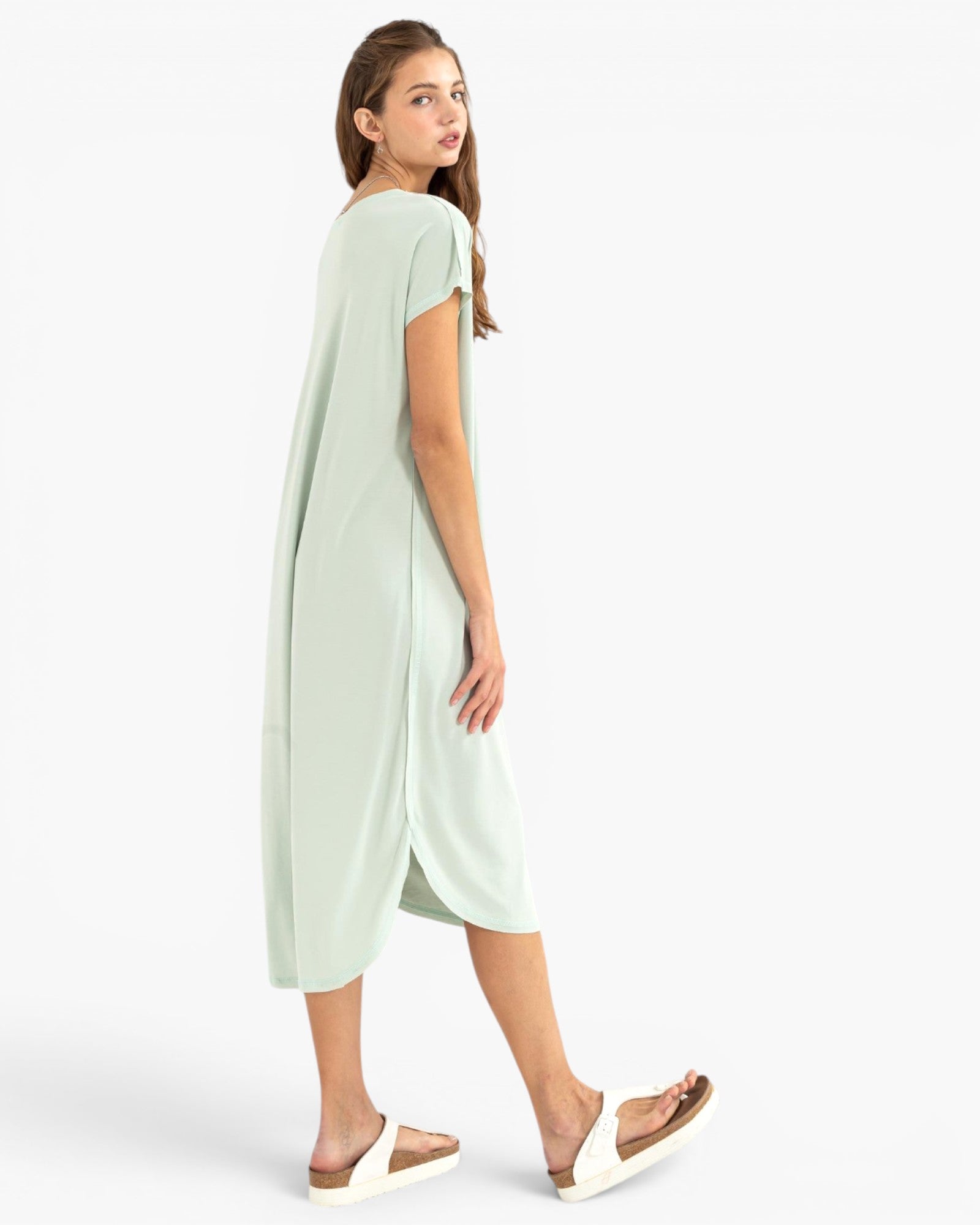A woman modeling a light mint green short-sleeve midi dress with a side slit, shown from a three-quarter back angle against a plain white studio background.