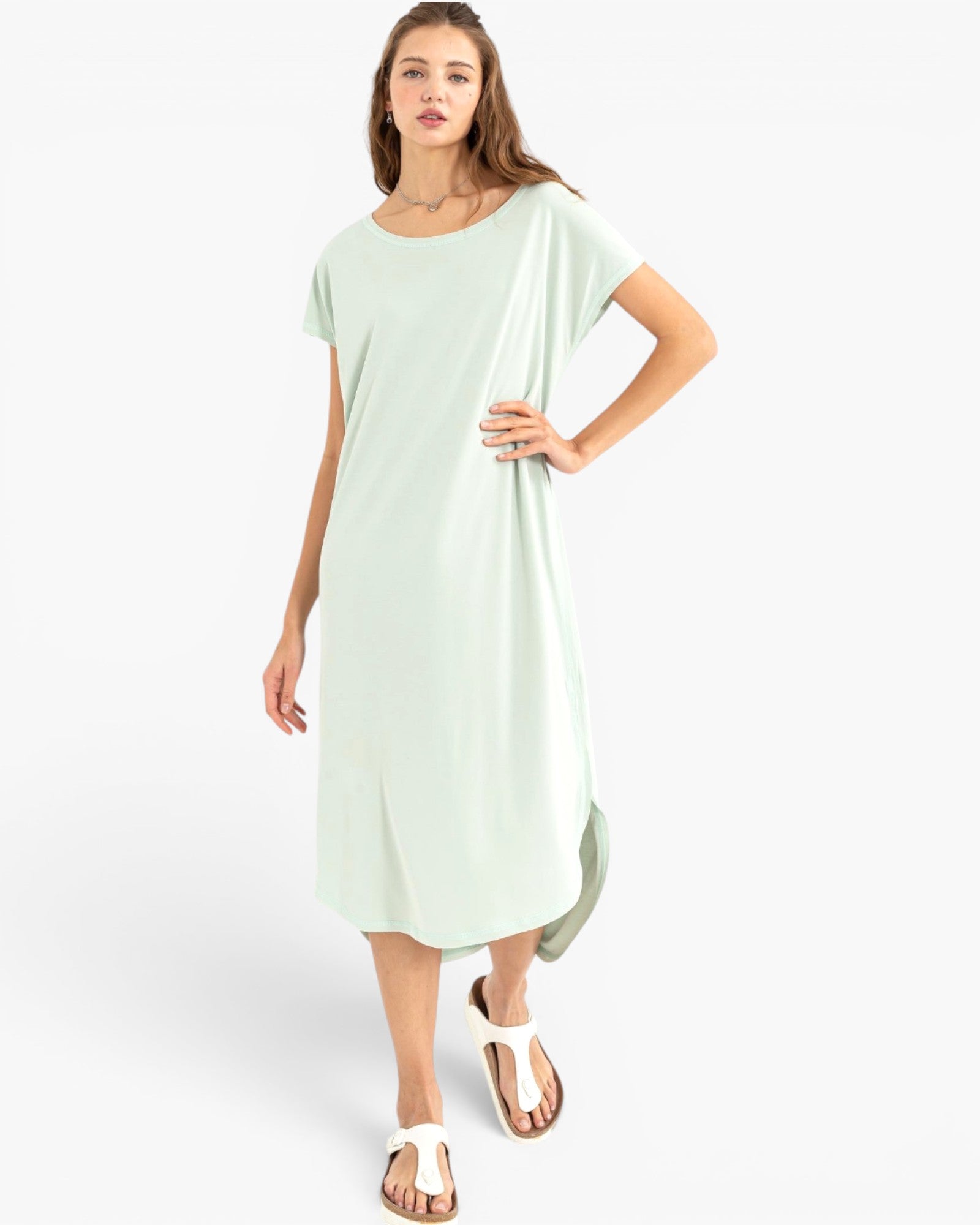 A woman modeling a light mint green short-sleeve midi dress with a relaxed, oversized fit, styled with white sandals against a plain white studio background.