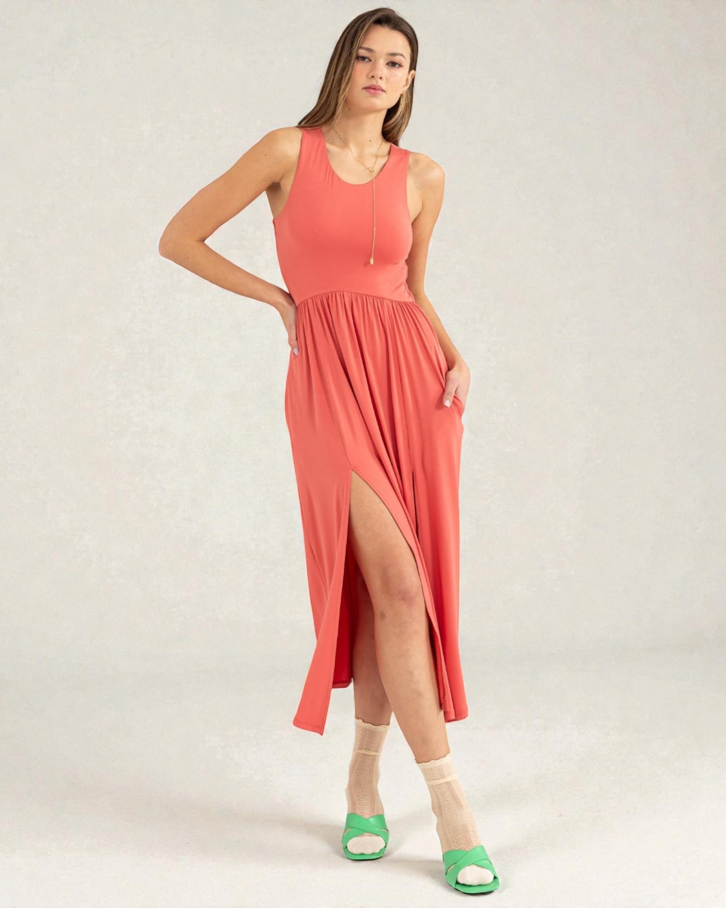 Woman wearing a coral dress with a slit on a plain background