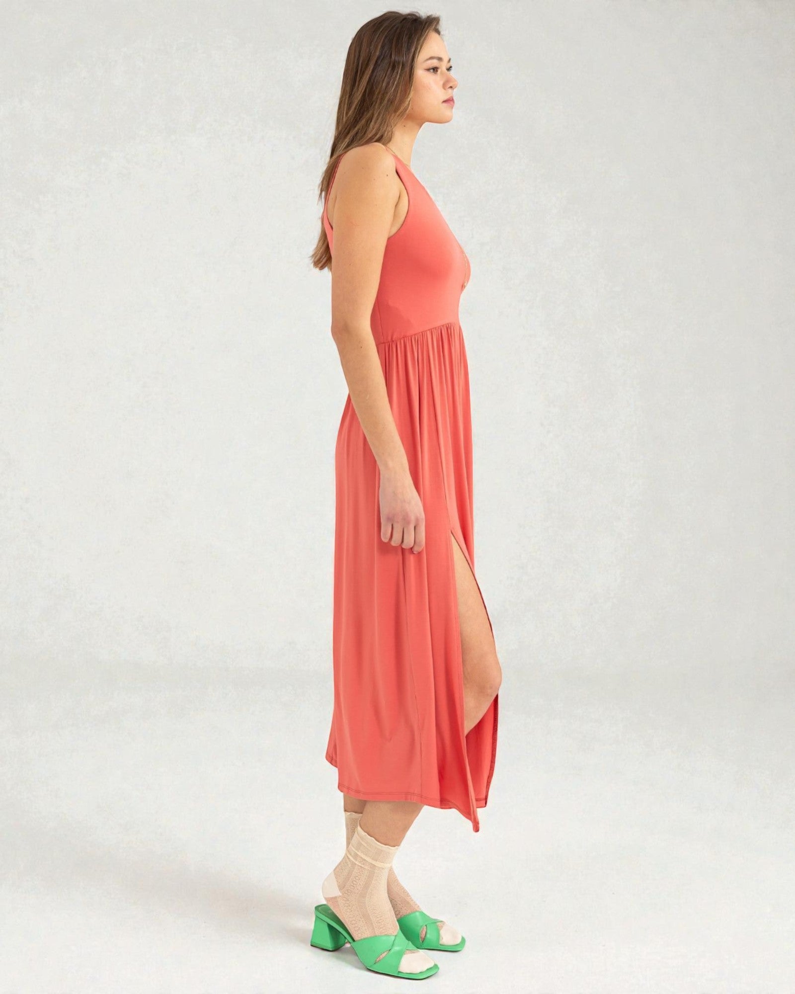 Woman wearing a coral dress with a slit on a white background