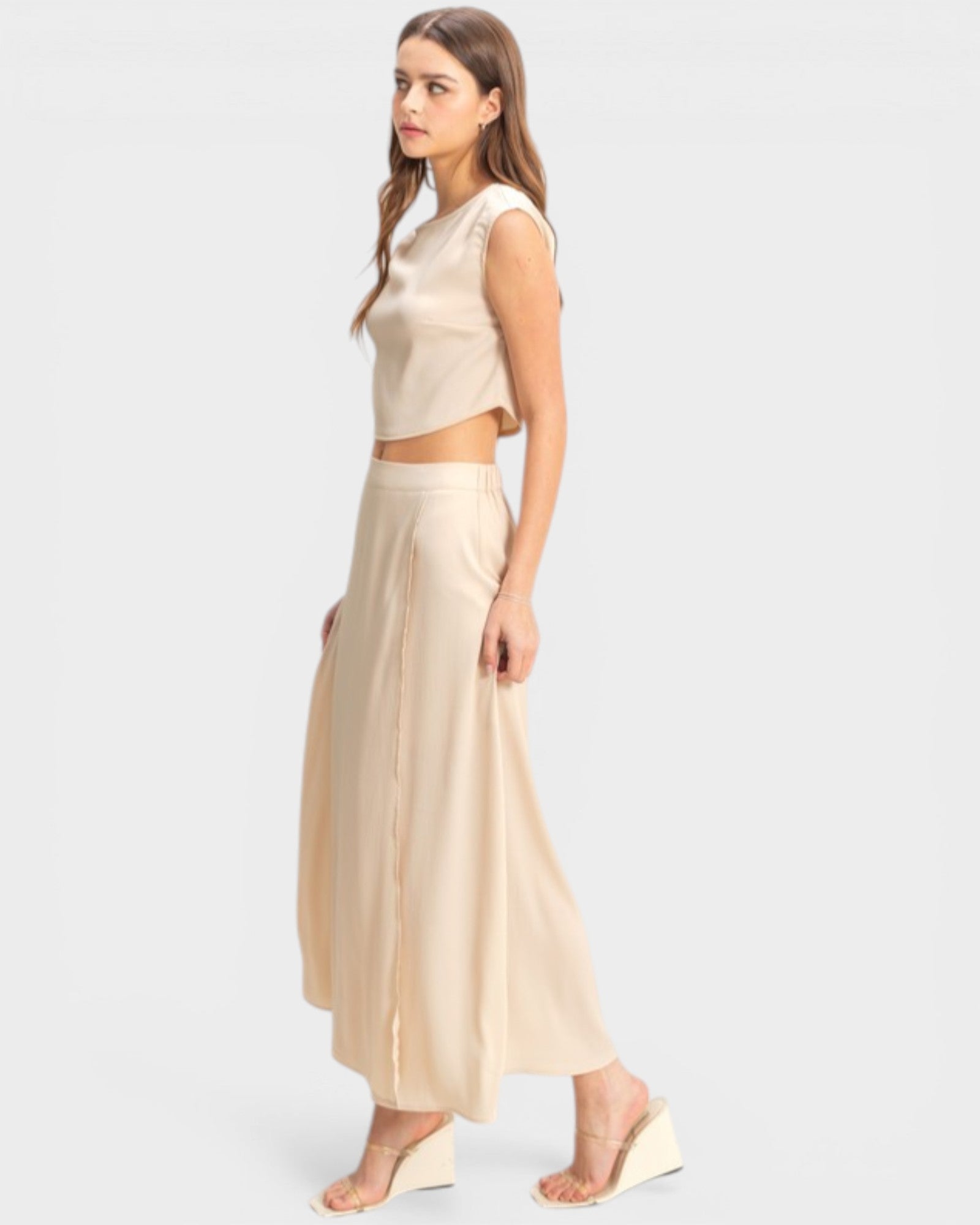 Woman wearing a beige sleeveless top and long skirt on a white background