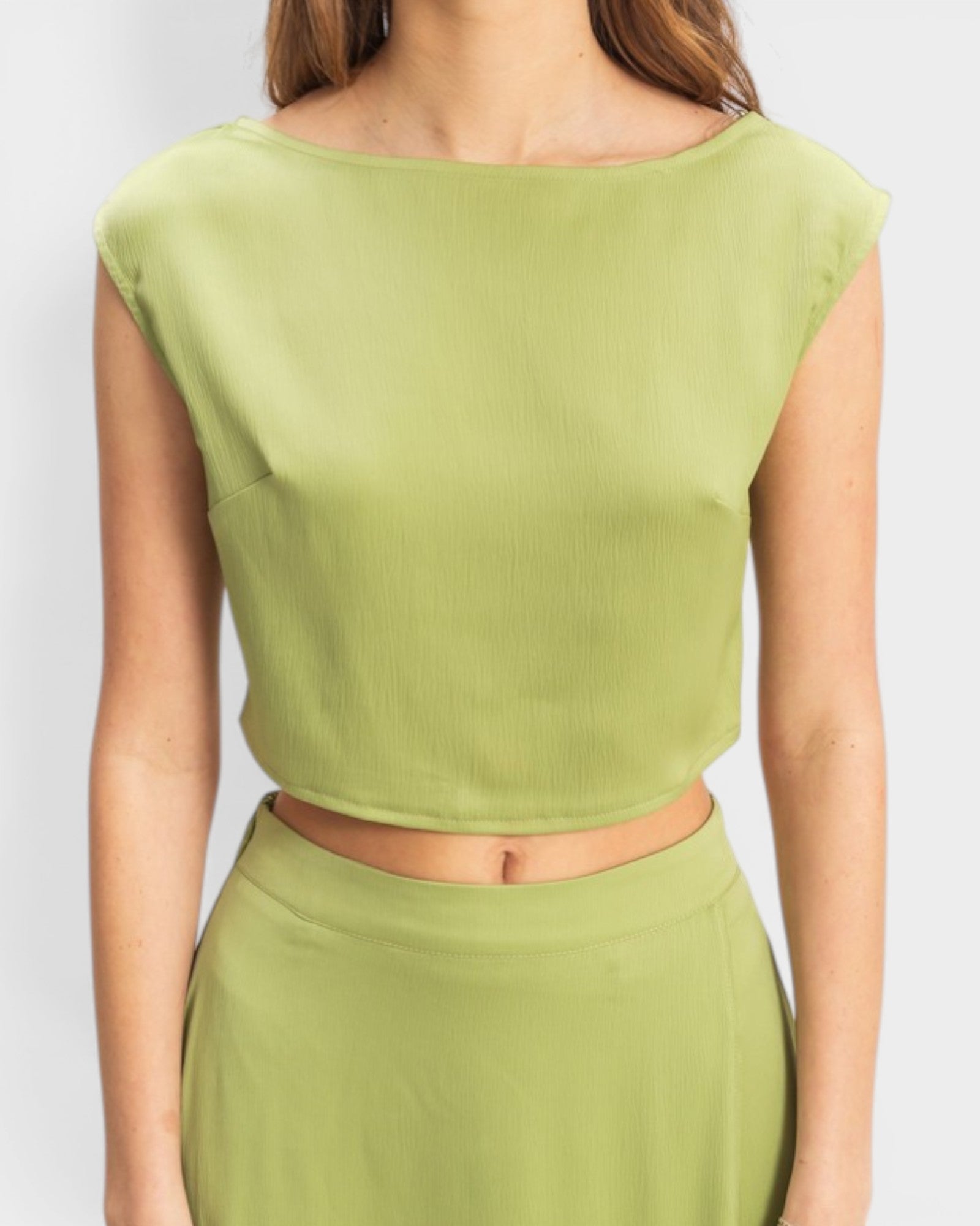 Green sleeveless top worn by a person on a white background