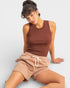 Woman wearing a brown ribbed tank top and beige shorts on a light gray background