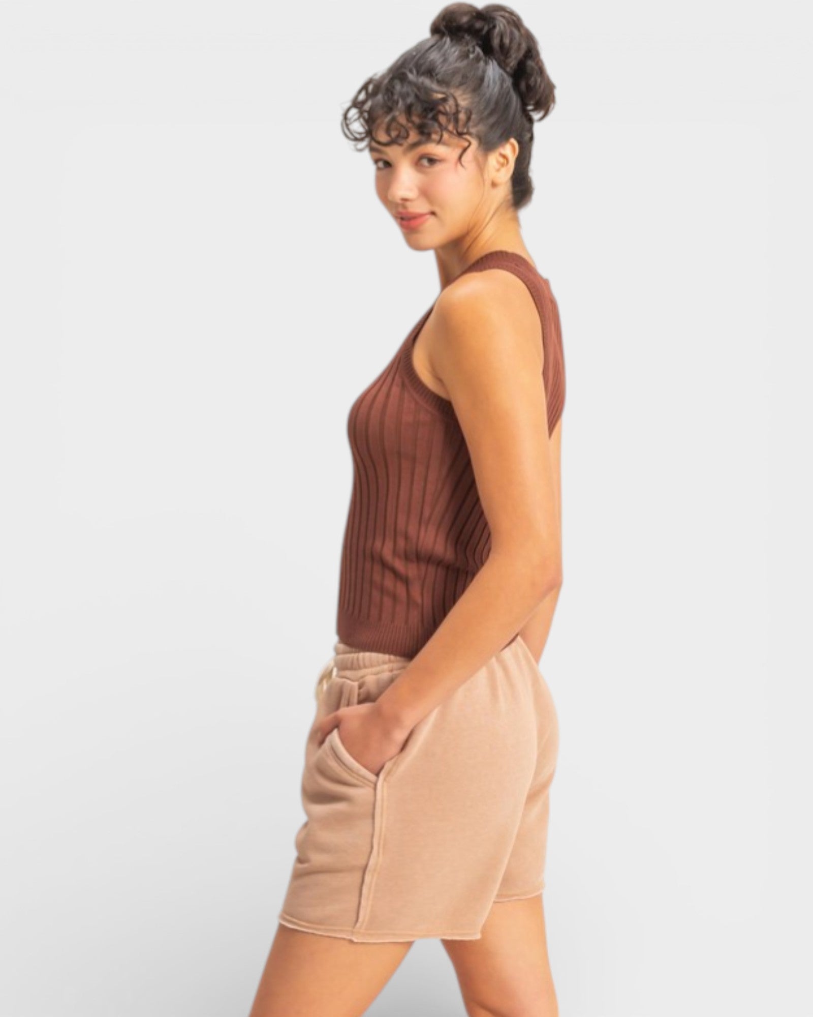 Woman wearing a brown sleeveless top and beige shorts on a white background