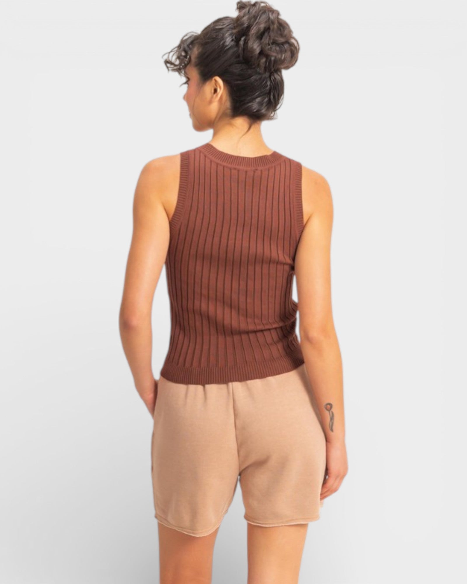 Person wearing a brown ribbed tank top and beige shorts on a white background