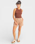 Woman wearing a brown ribbed tank top and beige shorts on a white background