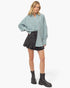 A model wearing a light blue-green and white vertically striped button-down shirt, a dark gray pleated mini skirt, and black platform ankle boots, photographed against a clean white background.