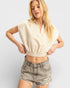 Woman wearing a cream ribbed crop top and denim shorts on a light gray background