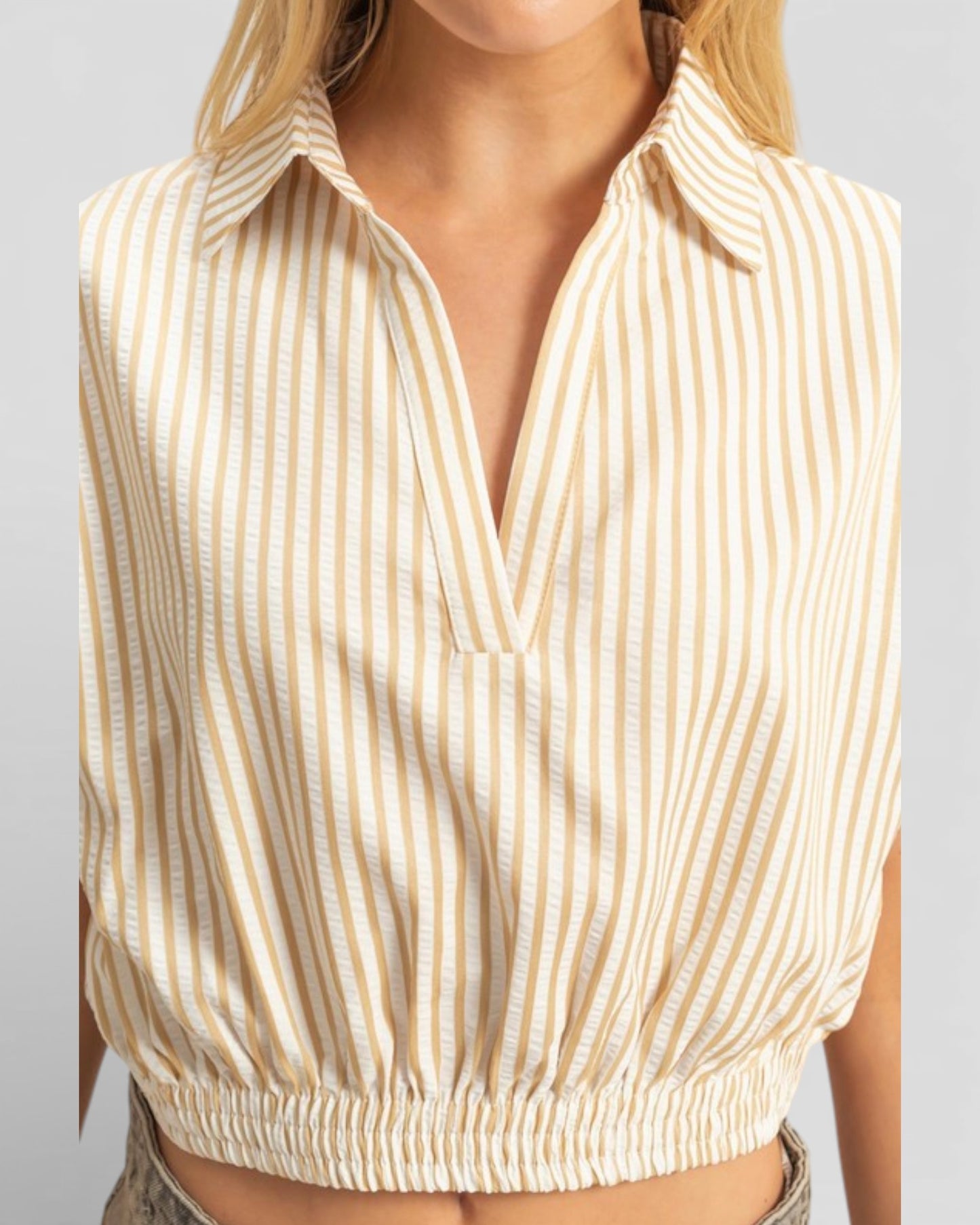 Beige and white striped sleeveless top worn by a person on a light gray background