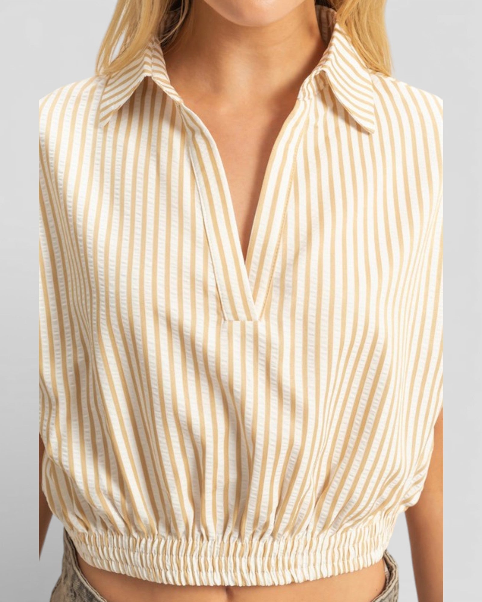 Beige and white striped sleeveless top worn by a person on a light gray background
