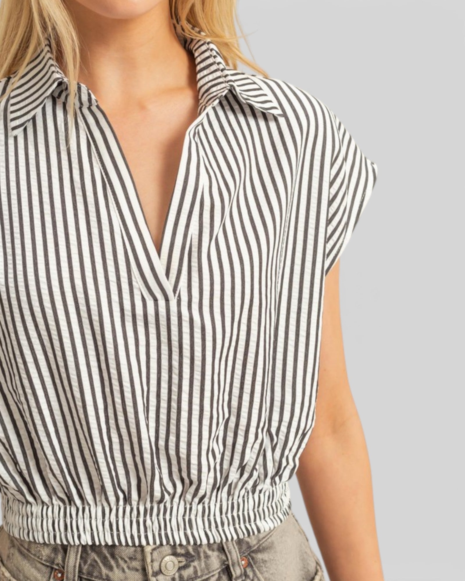 Black and white striped sleeveless top worn by a person on a gray background