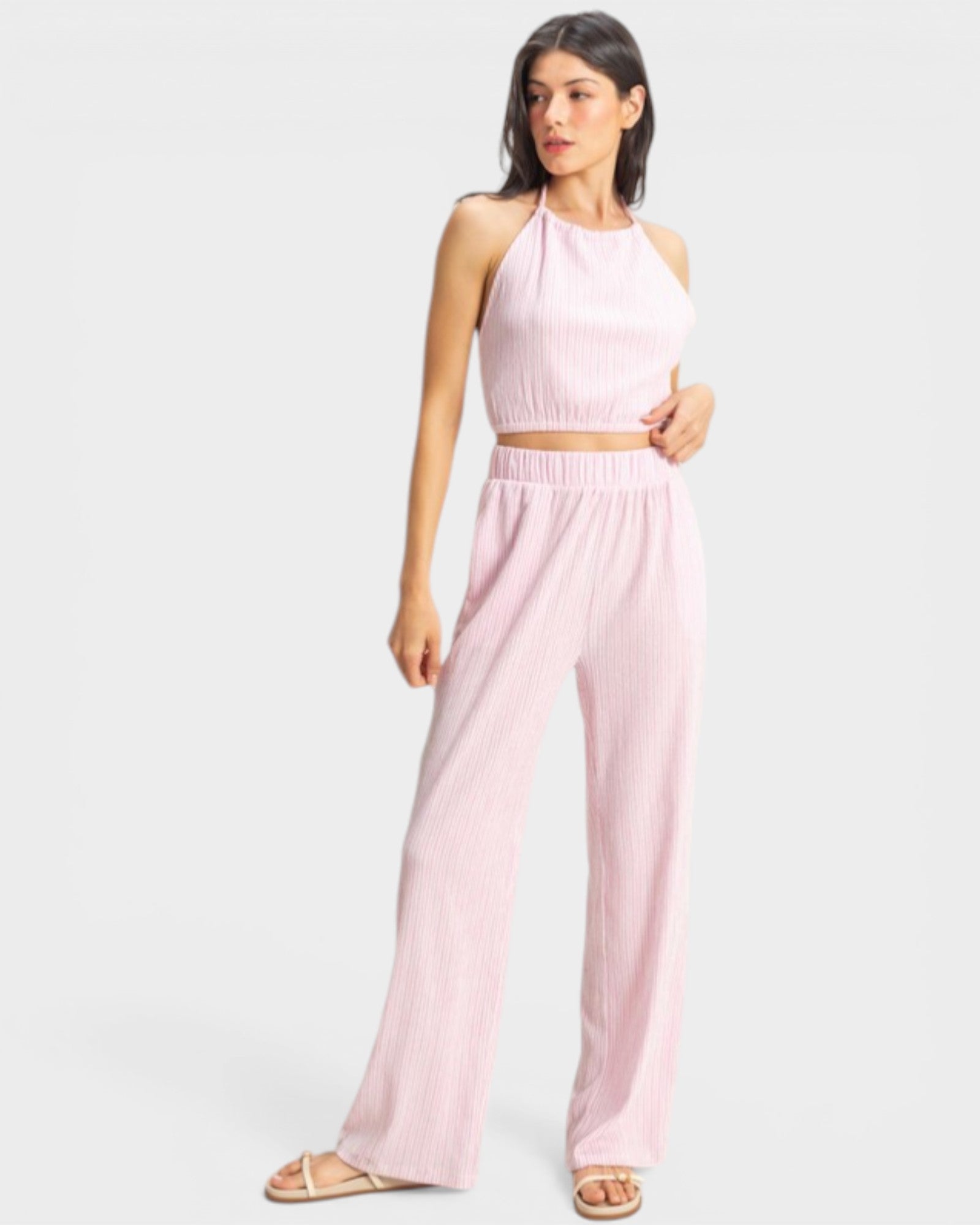 Woman wearing a pink one-shoulder top and wide-leg pants on a white background