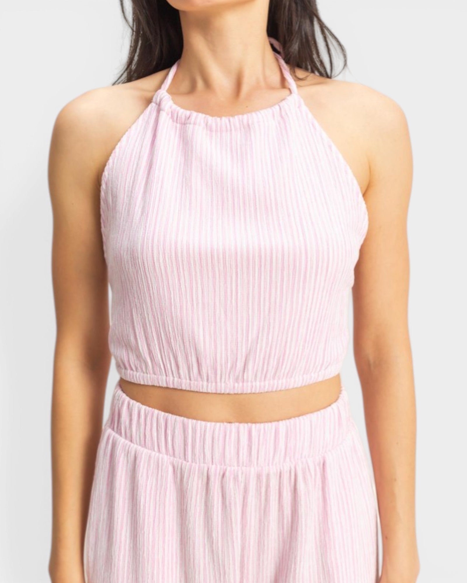 Woman wearing a light pink ribbed halter top and skirt set on a white background