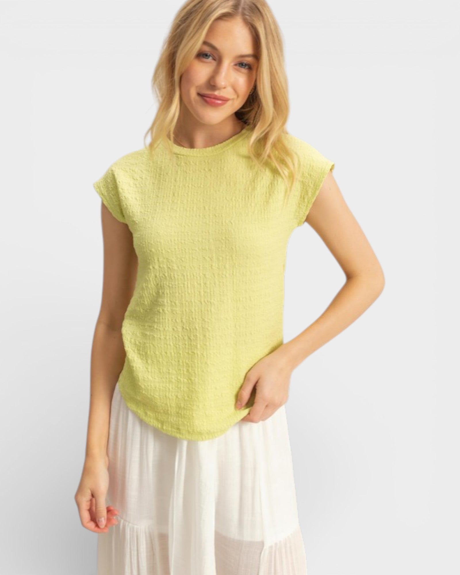 Woman wearing a light green sleeveless top and white skirt on a plain background