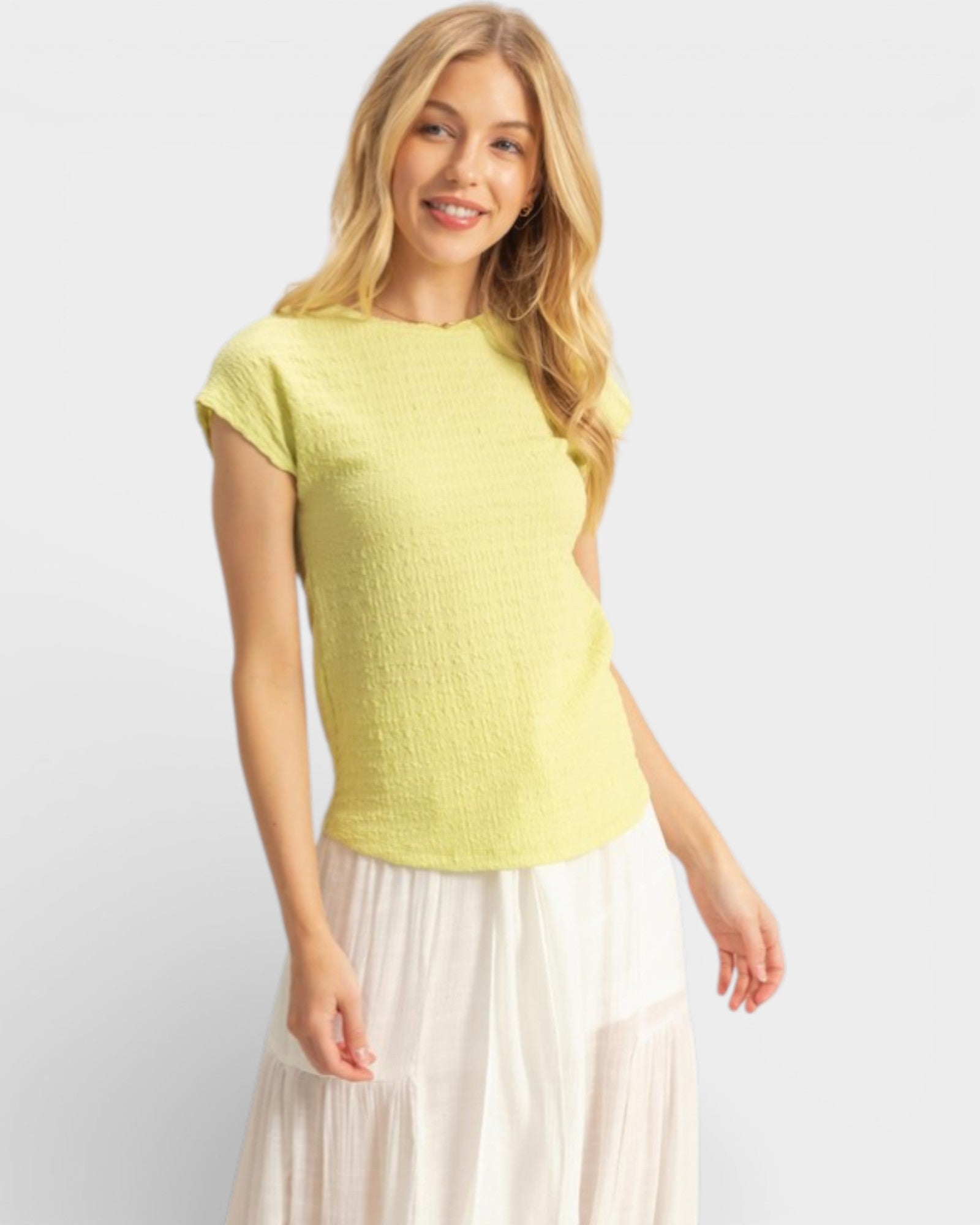 Woman wearing a light yellow textured top and white skirt on a plain background