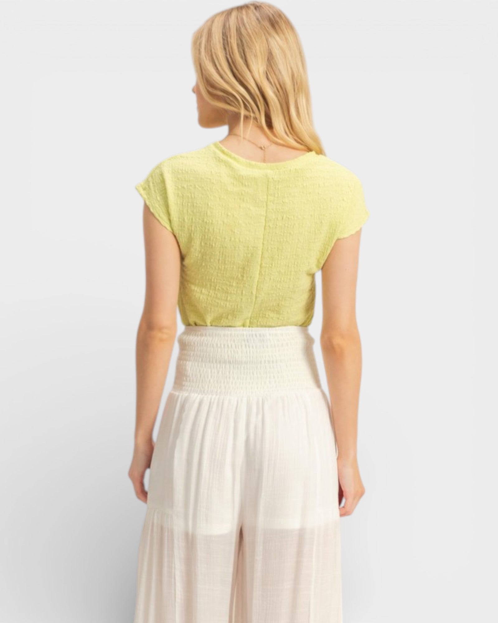 Woman wearing a yellow top and white pants on a light gray background