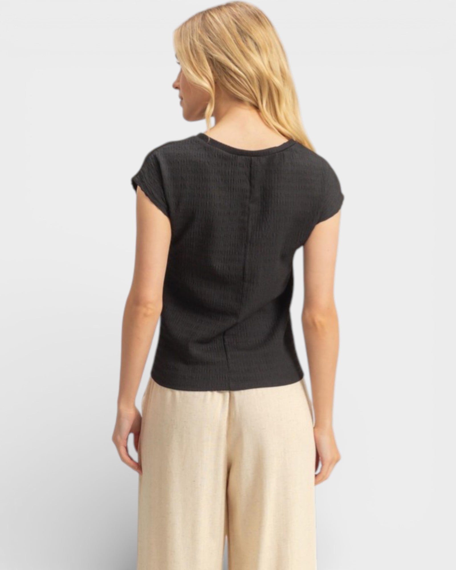 Woman wearing a black top and beige pants on a light gray background