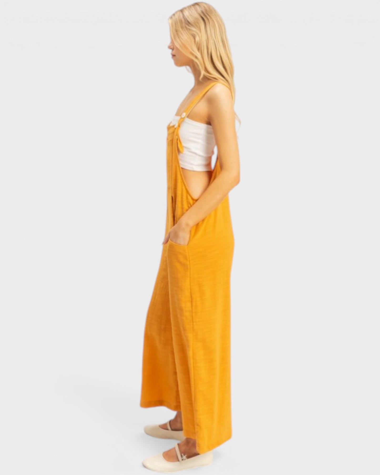 Woman wearing a mustard yellow dress with a white top on a light gray background